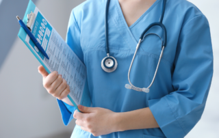 Healthcare professional in blue scrubs holding a clipboard and stethoscope.