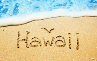 Hawaii written in sand with ocean waves, symbolizing Hawaii Medical College's commitment to culturally competent care.