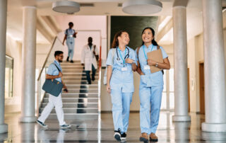 Healthcare students walking in campus hallway with scrubs and stethoscopes during hands-on medical training at Hawaii Medical College